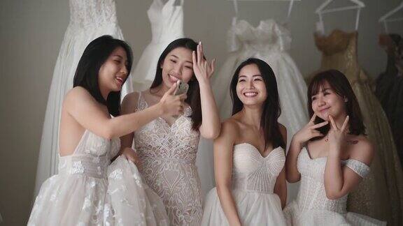 快乐顽皮的亚洲中国新娘和伴娘在婚纱店试婚纱时用智能手机自拍