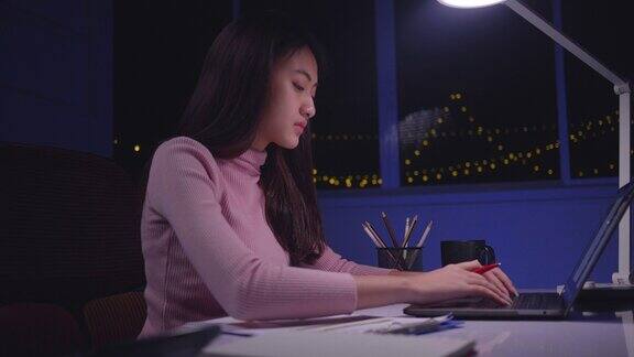 亚洲女性使用笔记本电脑工作到很晚晚上在家加班