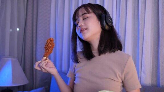 年轻的亚洲女性外卖吃垃圾食品鸡块鸡翅戴着耳机听音乐女性有乐趣享受快餐配送服务的餐饮理念