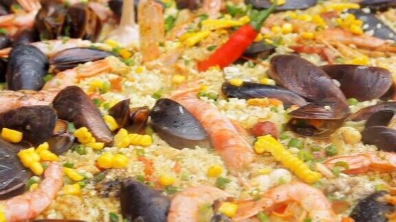 西班牙海鲜饭以黄米饭、虾和贻贝烹调平移相机街头食品节传统的西班牙食物米饭用海鲜煮近了