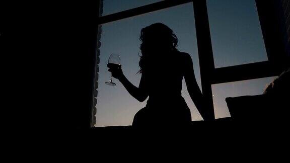 晚上在窗口摇晃酒杯的女士剪影