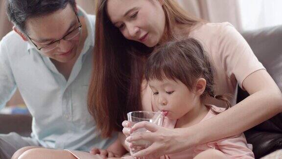 亚洲母亲给她的小女儿一杯牛奶一个可爱的蹒跚学步的小女孩喝着牛奶
