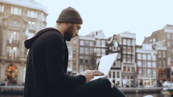 一个有创造力的人坐在街上拿着笔记本电脑移动办公室工作阿姆斯特丹老城大气的城市