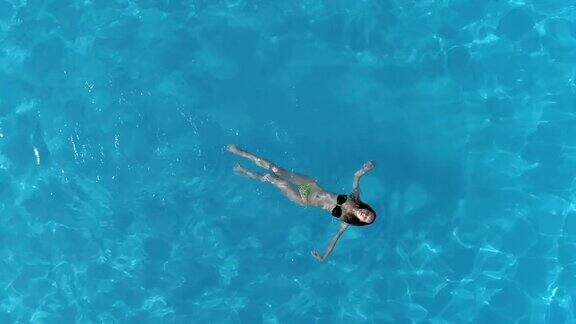 年轻女子浮在水面上在清澈的水池在夏天空中拍摄从飞行无人机