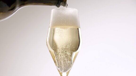 香槟酒从瓶子中倒入白色背景的漂亮玻璃杯中