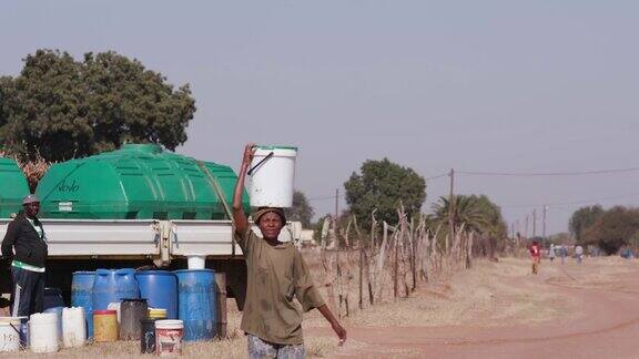 一位非洲妇女从水罐车里取水头上顶着水桶走回家