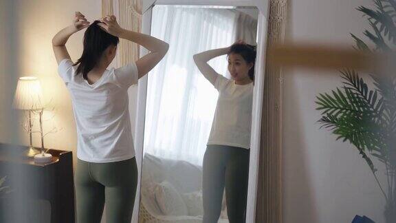 亚洲中国妇女系着她的头发准备瑜伽锻炼家庭锻炼在周末闲暇时间在镜子前