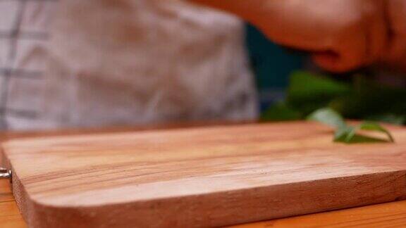 女手用菜刀在木板上切日本长洋葱或大葱或青葱女人正在家里的厨房里准备食物烹饪概念