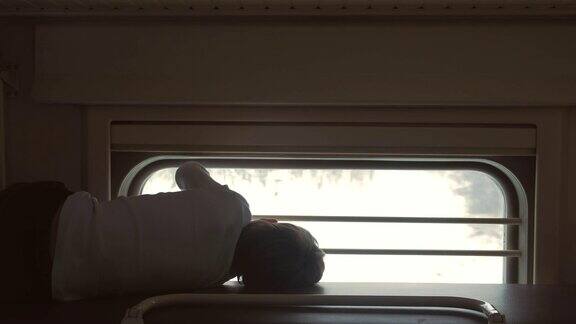 火车上的男孩躺在二等车厢的顶层架子上望着窗户后视图