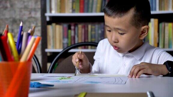 年轻的亚洲小男孩在纸上画画坐在桌子后面孩子做作业书架的背景