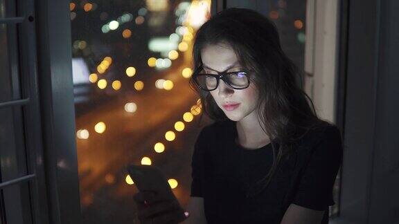 在夜晚城市的灯光背景下女孩手里拿着手机