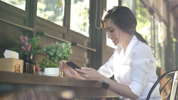 年轻的亚洲女商人在咖啡馆使用智能手机(慢镜头)