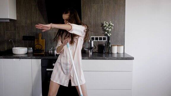 一个年轻的女人穿着睡衣在厨房里用拖把跳舞一个女士正在玩和唱歌