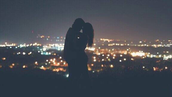 年轻的情侣在夜晚的城市背景下亲吻