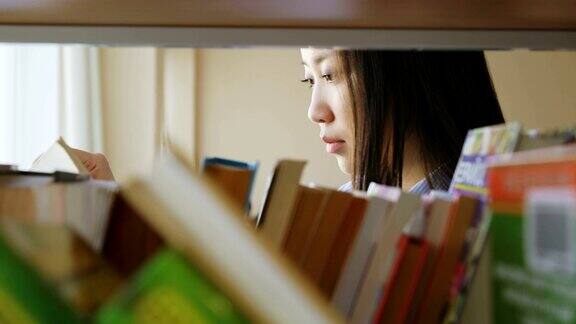 迷人的亚洲学生女孩站在书架旁边的书在大学图书馆拿书翻页阅读它