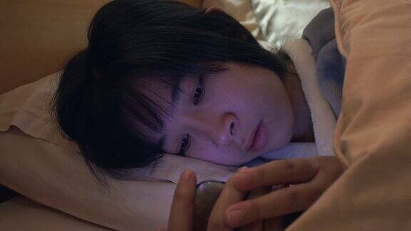 一个亚洲女人在晚上的卧室里用手机发短信