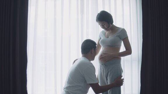 亚洲怀孕夫妇触摸和听肚子在客厅在家里