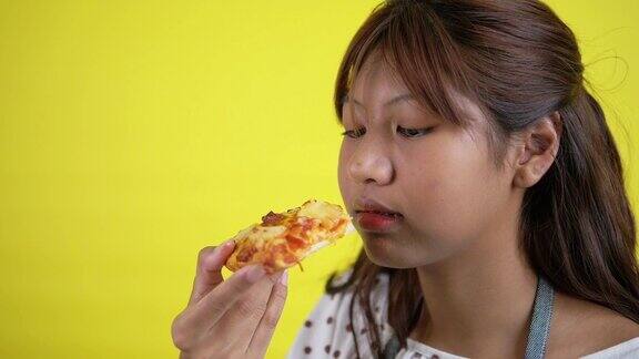 黄色背景下的亚洲青少年正在吃披萨