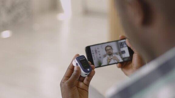 非洲男子坐着拿着手机拿着手指脉搏血氧计和男医生视频聊天