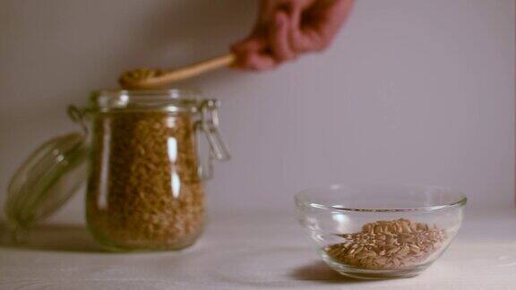 一个女人的手把燕麦从罐子里倒进碗里