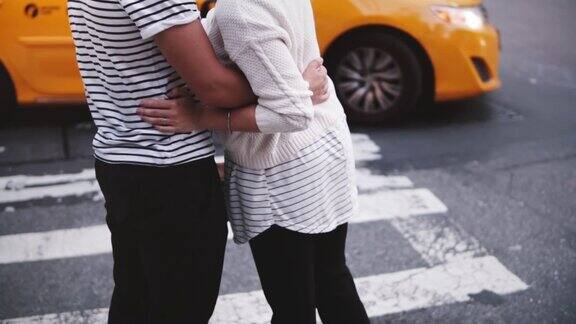 慢镜头:一对年轻的幸福浪漫的情侣站在一起拥抱在纽约的人行横道上汽车经过
