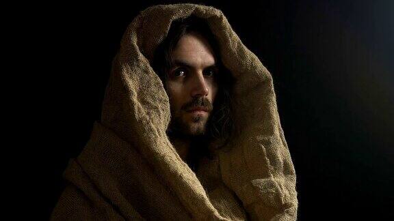 穿着长袍的耶稣基督在黑暗的背景下看着孤立的摄像机上帝之子