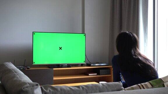 亚洲妇女看电视与绿色屏幕拍摄背后的模特肩膀