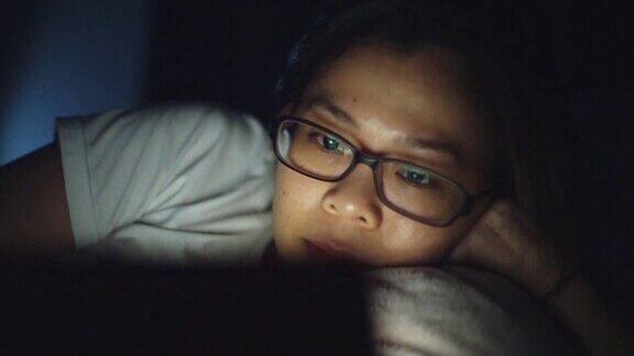 亚洲女人戴着眼镜晚上在卧室里看平板电脑