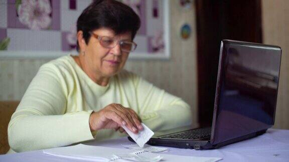 戴眼镜的老年妇女在家用笔记本电脑检查日常开支