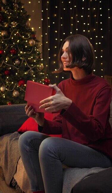 一个年轻漂亮的棕色头发的女人打开一个礼品盒里面的魔法灯照亮了她的脸背景是圣诞灯