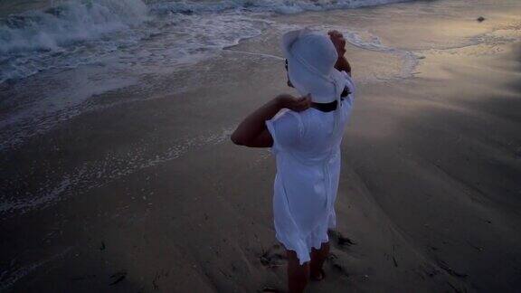 日落时分一位年轻美丽的女子站在海边穿着白裙子戴着白帽子她站在岸边眺望远方