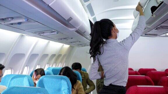 美丽的亚洲乘客戴着防护口罩在坐到座位上之前她把背包放在头顶的行李柜里准备起飞