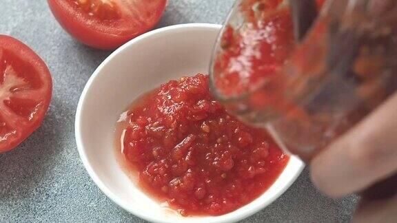 女人们用盘子从玻璃罐里舀出番茄酱自制的西红柿罐头