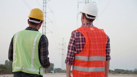 亚洲工程师和工头在日落的背景下讨论了一条输电线的建设