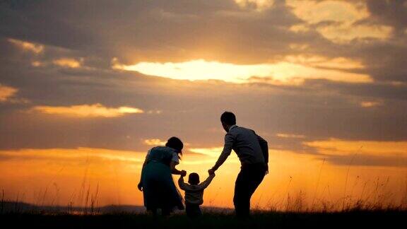 健康的一家人牵着爸爸妈妈的手在空中抚养宝宝一家人欢天喜地橘黄色的夕阳夏日