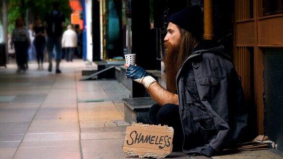 无家可归的人拿着“无耻”纸板在拥挤的街道上乞讨