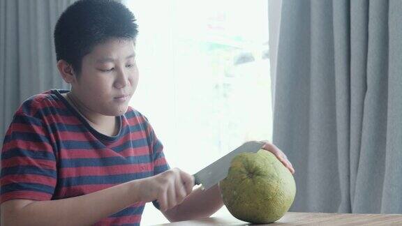 快乐的亚洲男孩坐在家里靠近窗户的地板上剥柚子生活理念