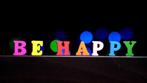 色彩缤纷的字‘快乐’从多色的木制字母前抽象模糊的灯光散景背景