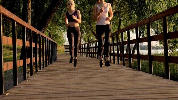两个年轻漂亮的女跑步者马尾辫在公园大桥上慢跑减肥健身模特跑步