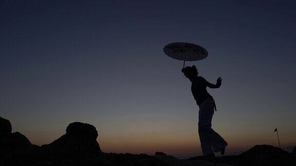 一个年轻女子的剪影走在岩石上带着日本伞