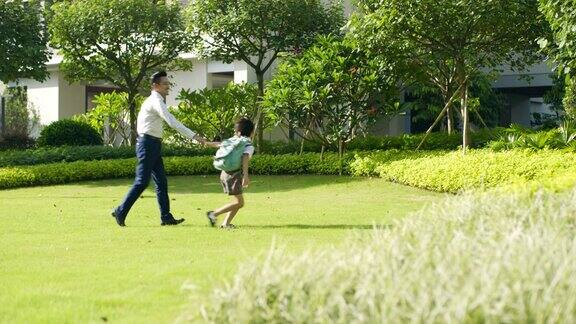 亚洲男孩通过花园和他的父亲去学校