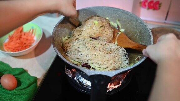 一个亚洲中国女性在家里烹饪中餐炒面在炉灶上烹饪平底锅