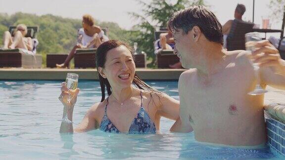 爱的成熟的夫妇在游泳池放松在暑假庆祝喝香槟
