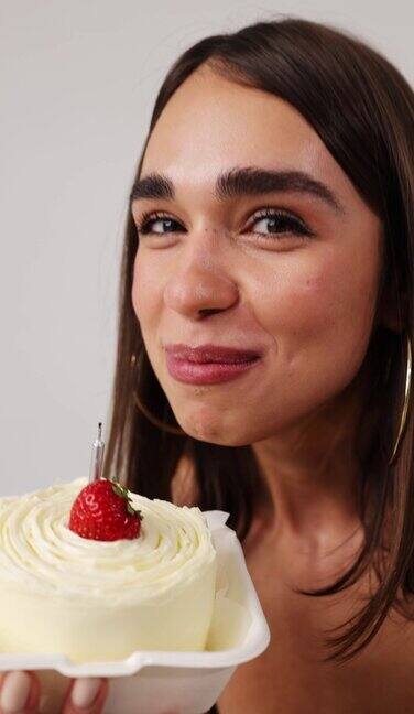 漂亮女孩用蜡烛和艾草舔蛋糕微笑着这个女孩正在庆祝她的生日垂直视频