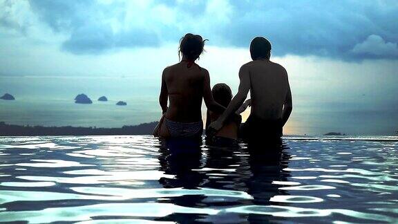 妈妈爸爸和他们的儿子拥抱坐在游泳池部分与无限的海景山顶在慢镜头1920x1080