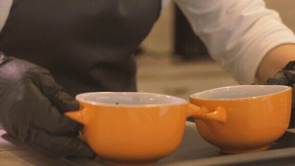 女厨师把两个盛有热汤的碗放在托盘上供餐厅使用