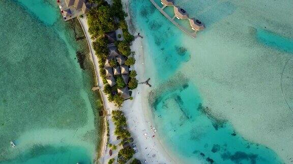 无人机摄像头正在降落到马尔代夫的热带岛屿那里有白色的沙滩和棕榈树阴影、平房和绿松石般的印度洋