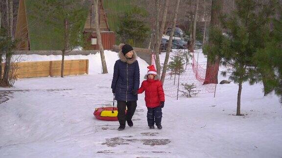 一个年轻的女人和她的小儿子有乐趣在油管在一个山区度假活动公园寒假