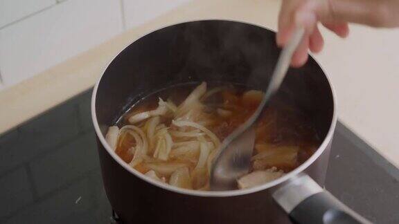 用不锈钢勺子搅拌锅里的猪肉和洋葱汤