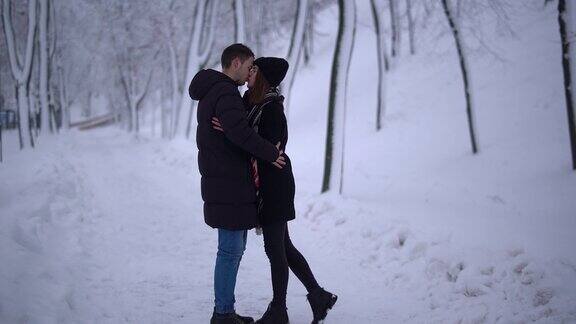 一对年轻的情侣在一个白雪覆盖的公园相遇并接吻